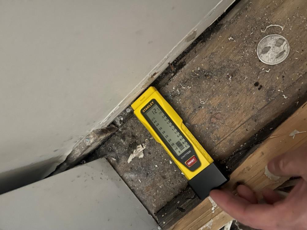 Moisture meter checking exposed wall framing after a ceiling pipe leak